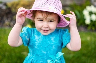 A happy toddler outdoors wearing a blue shirt and a pink hat
