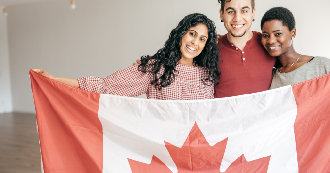 Two women and a man stand together holding a Canadian flag