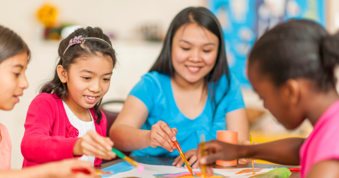 A Sunday school teacher paints with children at a table