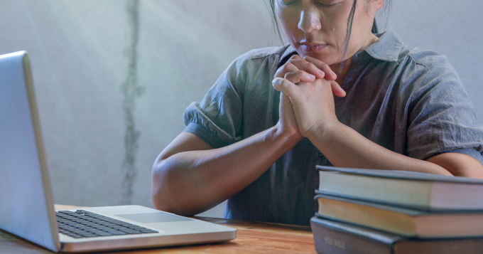 A woman prays in front of her laptop