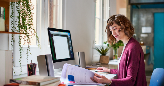 An office administrator sits in front of her computer while reviewing a paper report
