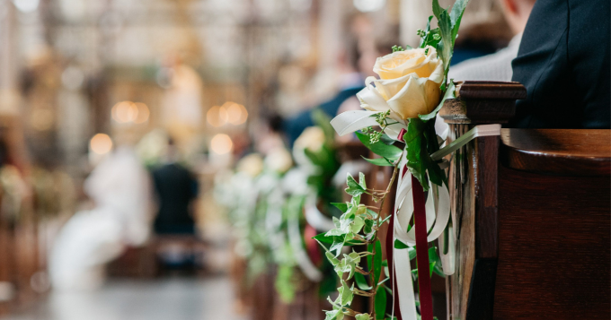 The arm of a dark wooden pew decorated with yellow roses
