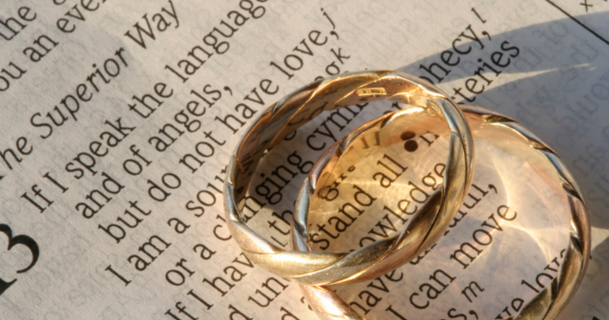 Two golden rings laid atop a Bible open to 1 Corinthians 13